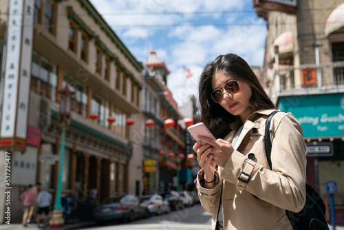 stylish asian Taiwanese woman visitor wearing sunglasses and checking travel info on the phone while touring Chinatown in san Francisco California usa on a sunny day.