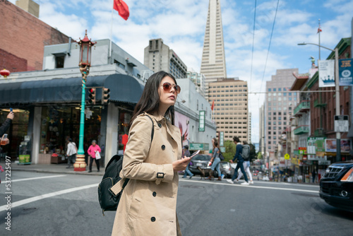 asian Taiwanese woman visitor holding phone using navigation app while crossing busy street in san Franciscoâs china town with chinese traditional lamp post at background