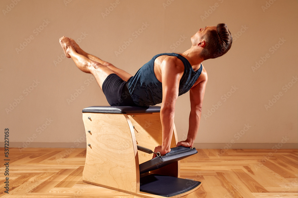 Handsome pilates male instructor performing stretching balance fitness exercise on small barrel equipment, at the pilates studio modern onterior indoor. Handsome pilates male instructor performing stretching balance fitness exercise on small barrel equipment, at the pilates studio modern onterior indoor.