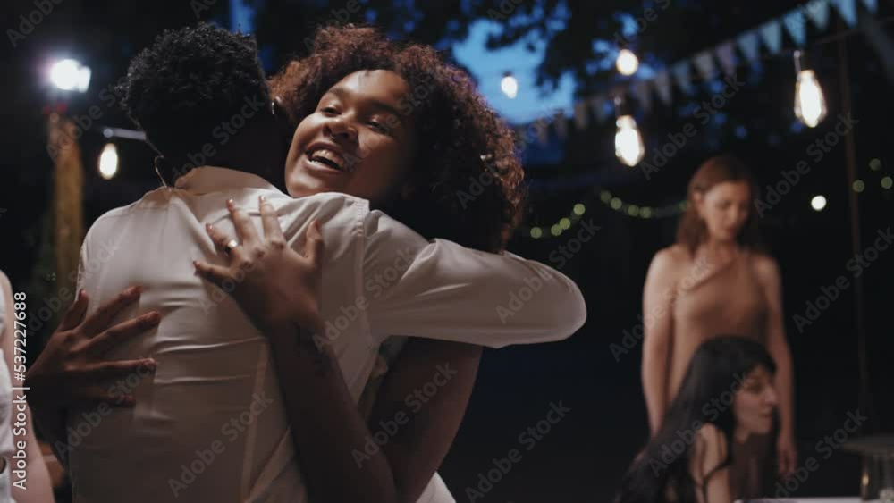 Young Black newlywed greeting her best friends with hugs then inviting them to festive table at wedding party in evening Young Black newlywed greeting her best friends with hugs then inviting them to festive table at wedding party in evening