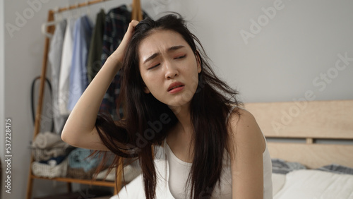 upset asian chinese female feeling migraine and coping with terrible hangover after getting up in the morning in the bedroom at home.