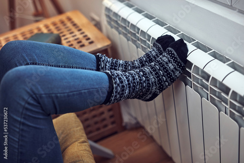 Woman heating feet on a chilly winter day, energy and gas crisis, cold room, heating problems.