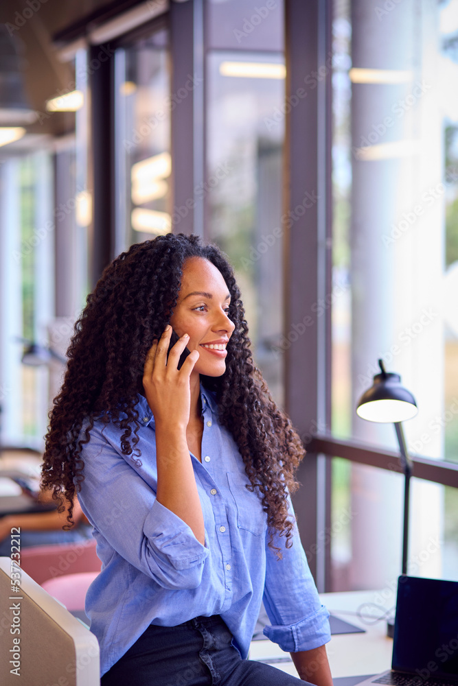 Businesswoman Standing By Partition In Open Plan Office Making Call On Mobile Phone Businesswoman Standing By Partition In Open Plan Office Making Call On Mobile Phone