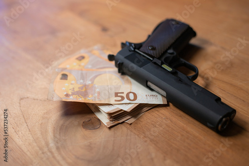 pistolet posé sur une table à côté d'une liasse de billets de banque de 50 euros