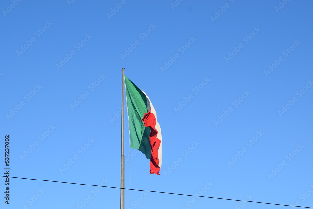 Fototapeta premium Large Italian flag flying against the blue sky