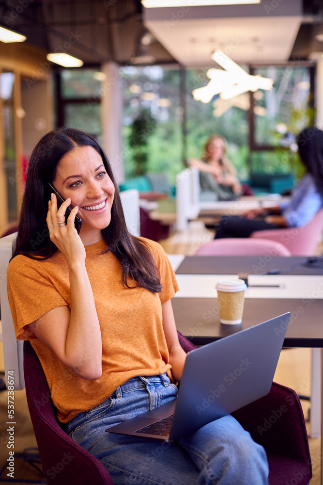 Businesswoman Sitting At Desk In Office Working On Laptop Talking On Mobile Phone Businesswoman Sitting At Desk In Office Working On Laptop Talking On Mobile Phone