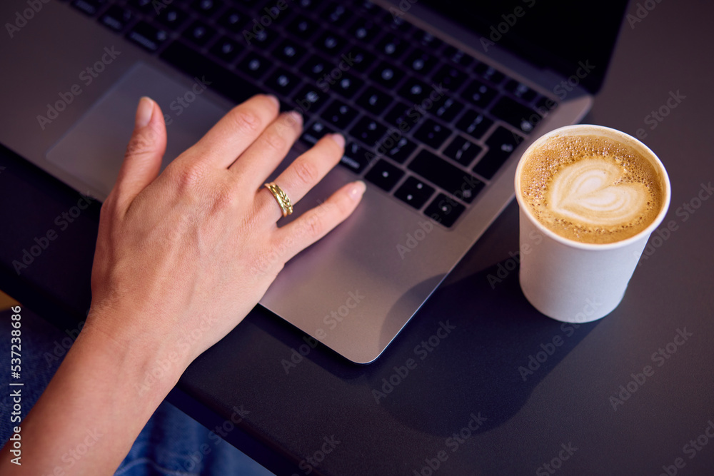Close Up Of Businesswoman Sitting At Desk In Office Working On Laptop With Takeaway Drink Close Up Of Businesswoman Sitting At Desk In Office Working On Laptop With Takeaway Drink