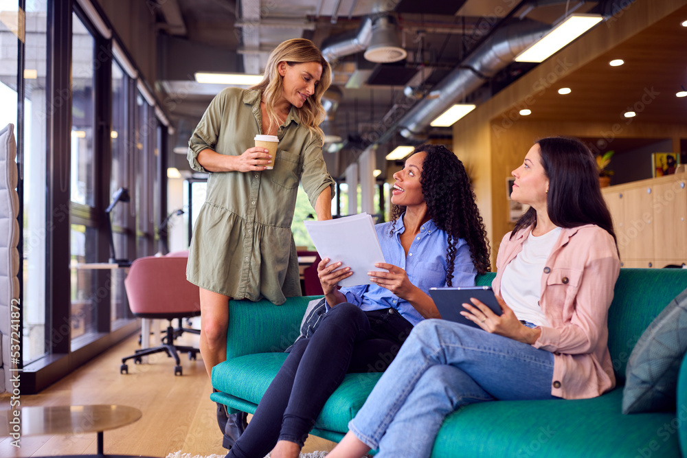 Businesswomen Having Informal Meeting In Breakout Seating Area Of Modern Office Businesswomen Having Informal Meeting In Breakout Seating Area Of Modern Office