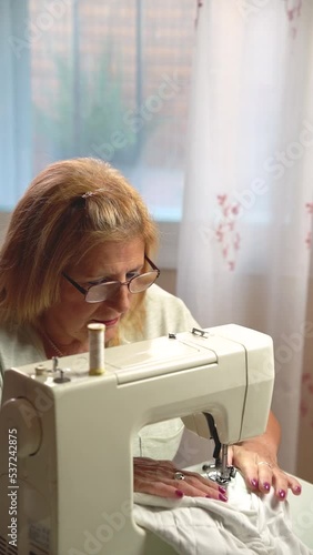 Older woman sewing at home with the sewing machine - concept of work and hobby