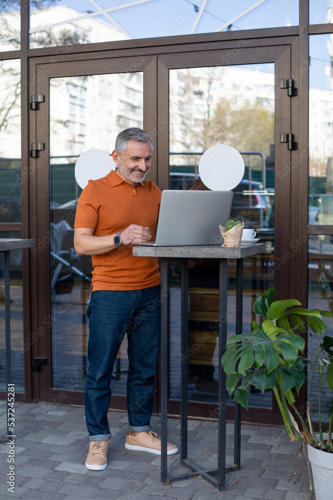 Mature man in orange shirt working online in the street cafe
