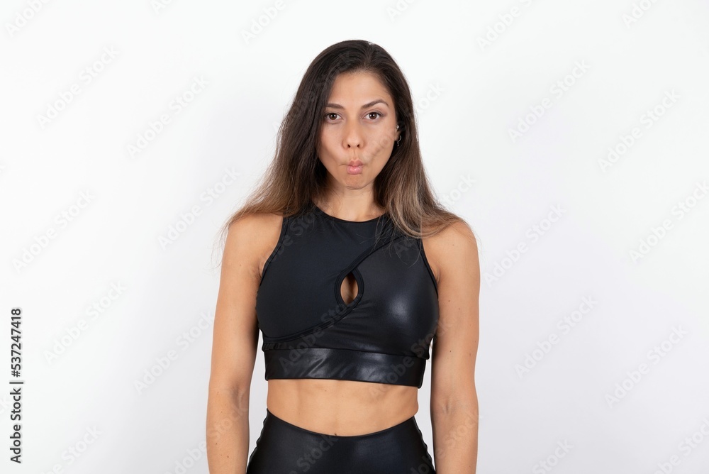 Shot of pleasant looking young beautiful woman wearing sportswear over white background, pouts lips, looks at camera, Human facial expressions Shot of pleasant looking young beautiful woman wearing sportswear over white background, pouts lips, looks at camera, Human facial expressions