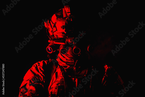 Half length, low key studio shoot of army soldier, marine infantryman in mask, camo uniform, equipped modern ammunition, armed service rifle standing in darkness with night vision device on helmet