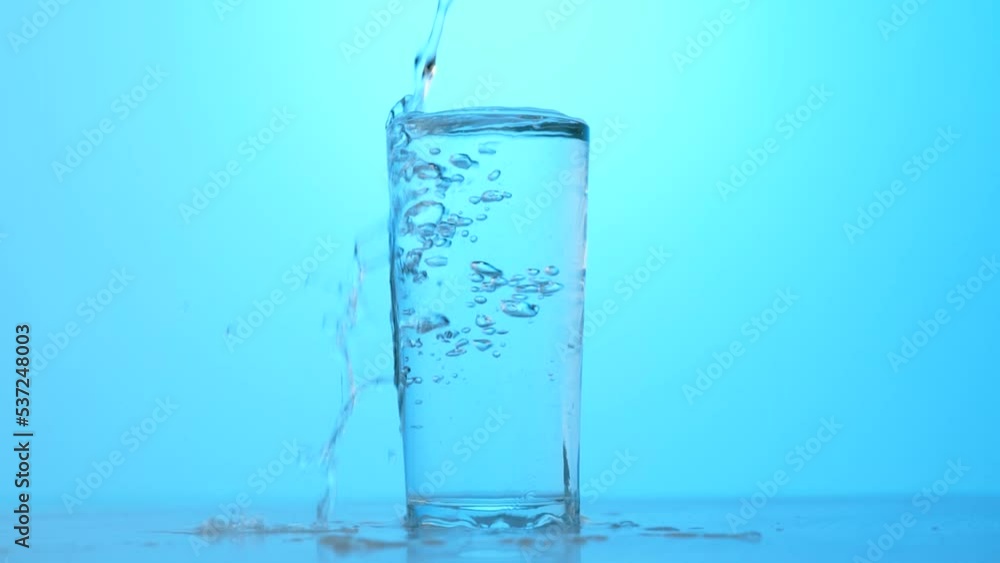 pour clean water into a transparent glass on a blue background, slow motion pour clean water into a transparent glass on a blue background, slow motion