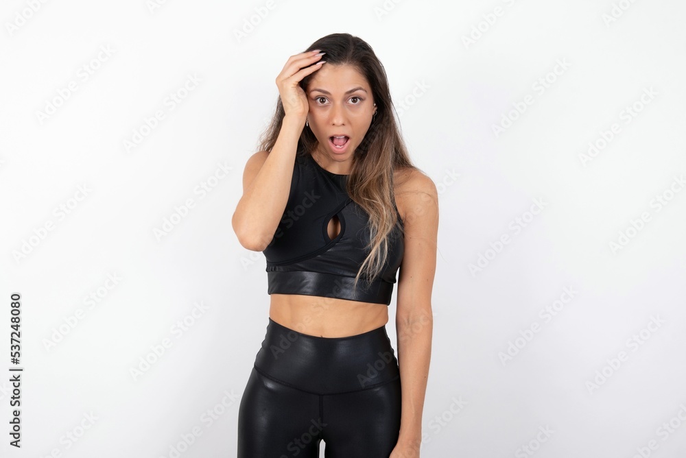 Embarrassed young beautiful woman wearing sportswear over white background with shocked expression, expresses great amazement, Puzzled model poses indoor Embarrassed young beautiful woman wearing sportswear over white background with shocked expression, expresses great amazement, Puzzled model poses indoor
