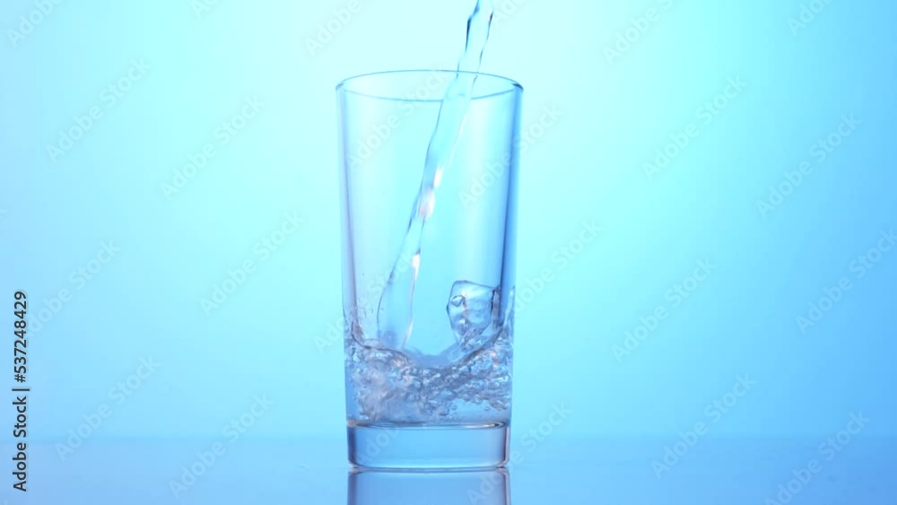 pour clean water into a transparent glass on a blue background, slow motion pour clean water into a transparent glass on a blue background, slow motion