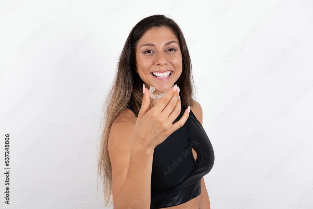 young beautiful woman wearing sportswear over white background holding an invisible aligner ready to use it. Dental healthcare and confidence concept. young beautiful woman wearing sportswear over white background holding an invisible aligner ready to use it. Dental healthcare and confidence concept.