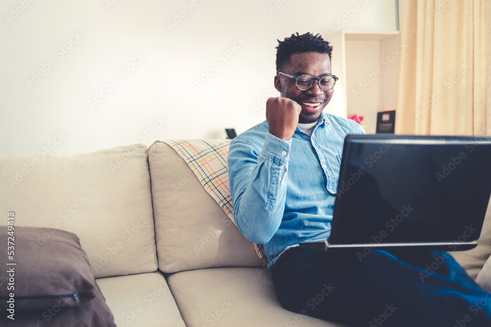 Success at work, good deal. African-American men looks at the laptop screen, screams excitedly and raises his fists in a victory gesture. Success at work, good deal. African-American men looks at the laptop screen, screams excitedly and raises his fists in a victory gesture.