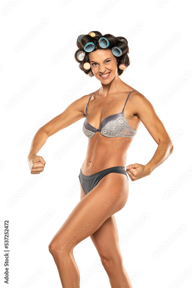 Happy woman in underwear with hair curlers on her head showing biceps and perfect body on a white background Happy woman in underwear with hair curlers on her head showing biceps and perfect body on a white background