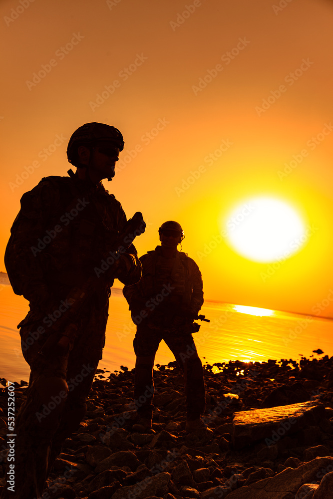 Army soldiers with rifles orange sunset silhouette in action during raid on the river coast
