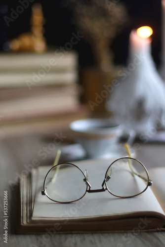 Stack of vintage books, cup of tea or coffee, lit candles, reading glasses and chess pieces on wooden table. Dark academia concept. Selective focus. © jelena990