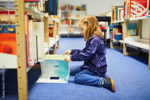 4 year old girl sitting on the floor in municipal library and reading a book photo