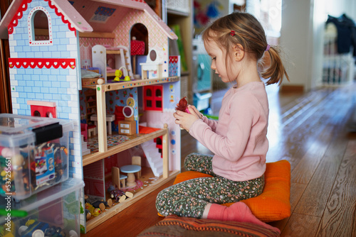 Adorable preschooler girl having fun with doll house in playroom at home