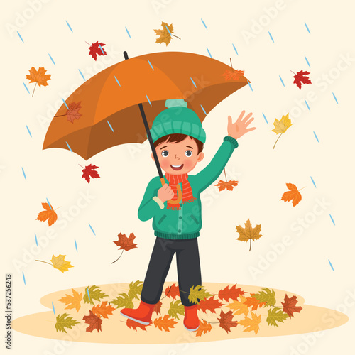 happy little boy holding umbrella under rain with fallen leaves in autumn 