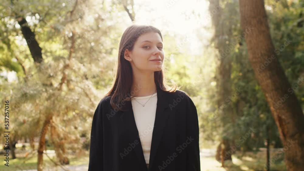 Attractive caucasian brunette female model turns to the camera, smiles, crosses her arms while standing outdoors Attractive caucasian brunette female model turns to the camera, smiles, crosses her arms while standing outdoors