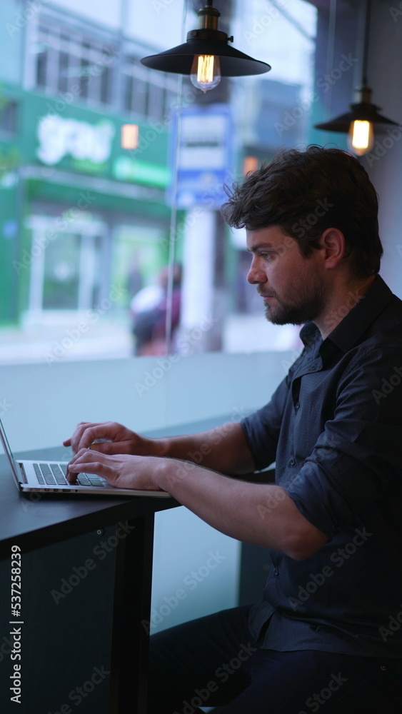 Fototapeta premium Young man typing on computer laptop seated at cafe workplace. Entrepreneur works remotely. Vertical Video
