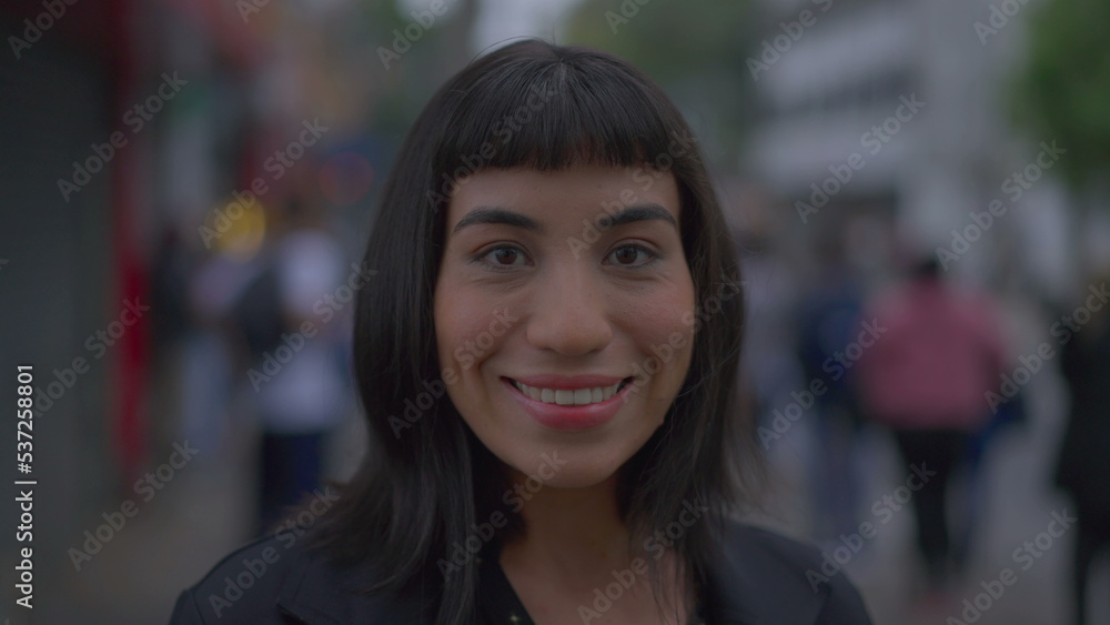 Happy woman with indigenous traits standing in urban street sidewalk looking at camera smiling. South American latina female person