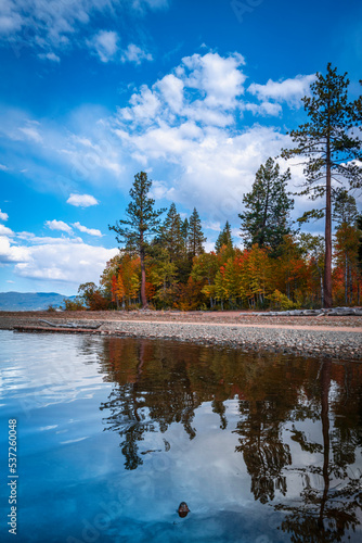 Tranquil Lake Tahoe with serene water reflections of the pine trees, autumn foliage, glacial rocks, and dramatic clouds on Baldwin Beach near Taylor Creek in Northern California