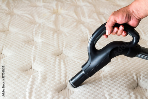 A hand is cleaning the surface of the bed with a vacuum cleaner