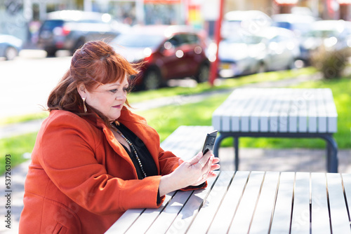 Woman with unsure neutral expression looking at mobile phone in park photo