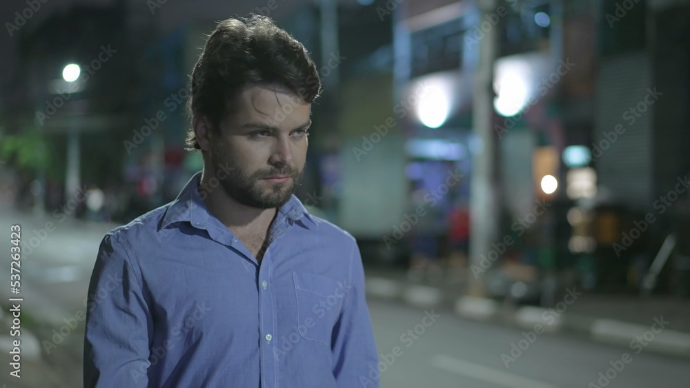 Fototapeta premium Pensive young man walking in city street at night. Thoughtful person walks in urban sidewalk in mental reflection in the evening