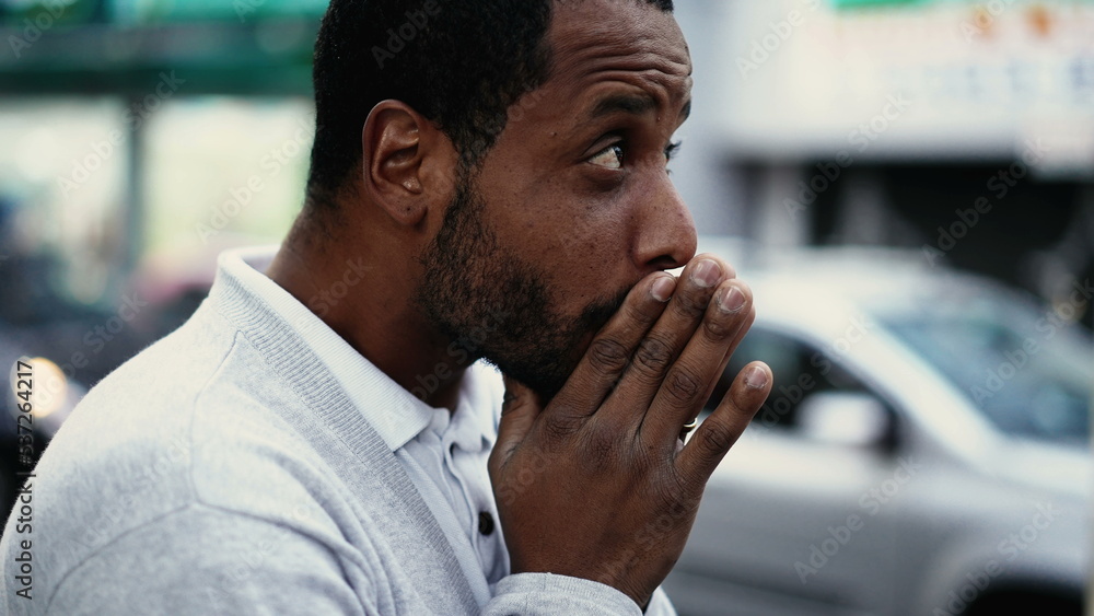 Fototapeta premium One spiritual young black man praying in street having HOPE and FAITH. African American prays in city urban sidewalk