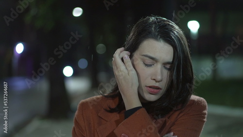 One lonely young woman walking at night in drizzle rain in downtown street. Sad depressed person with arms crossed walks in evening stroll with worried expression © Marco