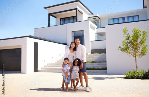 Portrait, real estate and happy family moving into their new luxury home, house or property in summer. Happy parents and children standing with a smile outdoor with building investment or purchase
