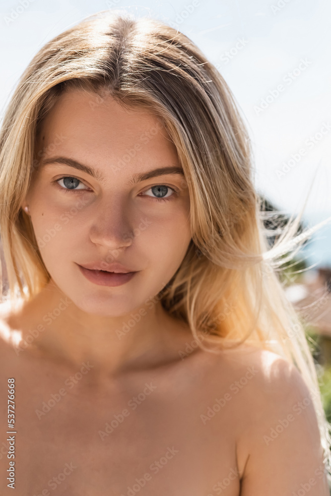 portrait of young blonde woman with bare shoulder looking at camera outside. portrait of young blonde woman with bare shoulder looking at camera outside.