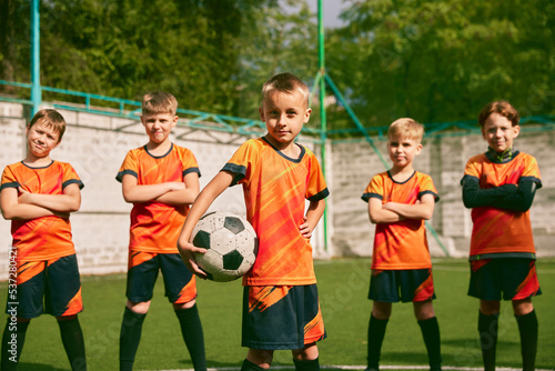 Fototapeta Naklejka Na Ścianę i Meble -  Future football champions. Little boys, kids in sports uniform posing with ball at soccer school stadium. Concept of sport, studying, achievements, success