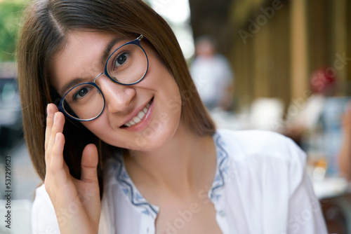 Portrait of young smiling woman wearing stylish eyeglasses looking at camera sitting in cafe. Vision concept 