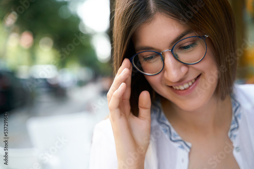 Portrait of the young smiling woman wearing stylish eyeglasses sitting in cafe, selective focus. Human emotions concept 