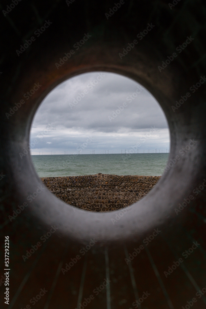 View out to seas and wall of a pier taken thought a hole cut out from a stone sculpture