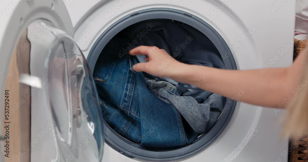 Close-up on the hands of a woman putting clothes into a washing machine. The filled interior of the drum, inserting laundry, closing the door and turning on the program. Close-up on the hands of a woman putting clothes into a washing machine. The filled interior of the drum, inserting laundry, closing the door and turning on the program.