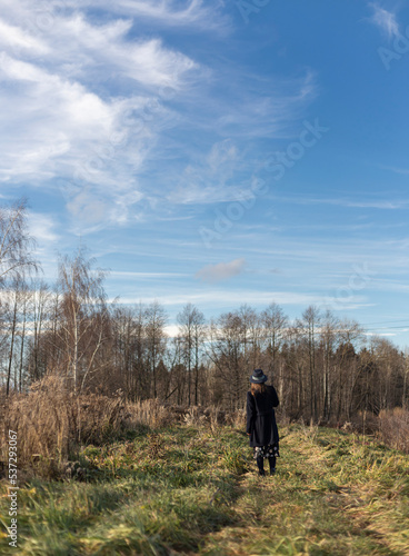 Young woman in dark coal and hat exploring autumn nature landscape standing backside