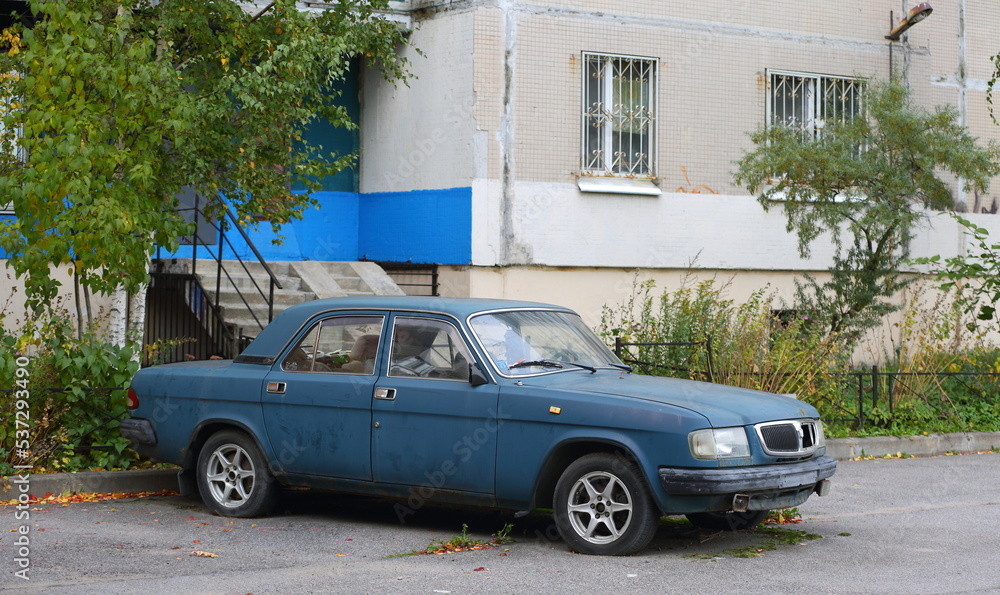 An old rusty blue car is parked near a residential building, Kollontai Street, St. Petersburg, Russia, October 2022