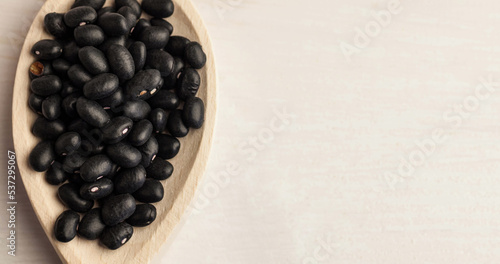 High angle view of black beans in wooden plate over white table, copy space