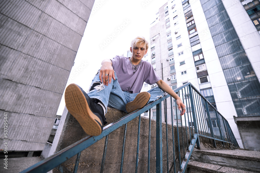 A teenage boy is sitting in an urban exterior surrounded by buildings.