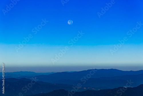 Moon and day in bright clouds before sunset. Moon in the blue sky. Moon and day with mountain. Day moon in summer time. Mountain and moon day with blue sky.