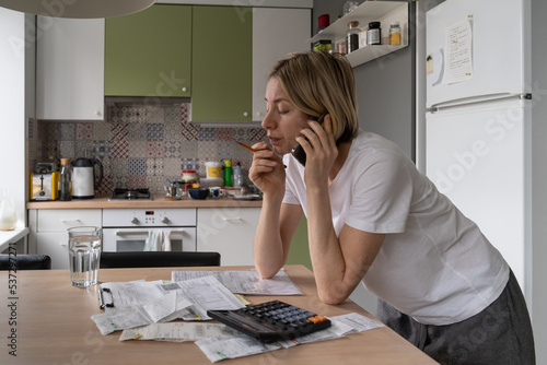 фотографія Mature woman looks with annoyed expression on bills lying on table