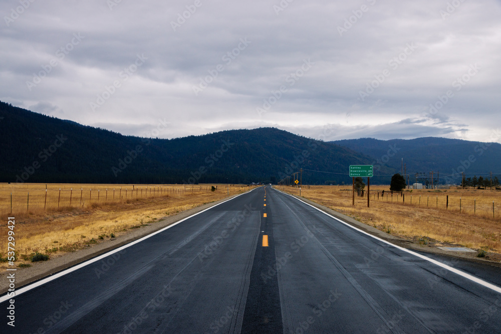 Empty road in America in a cloudy day. Empty road in California going through a yellow field with a view of the mountains in a distance